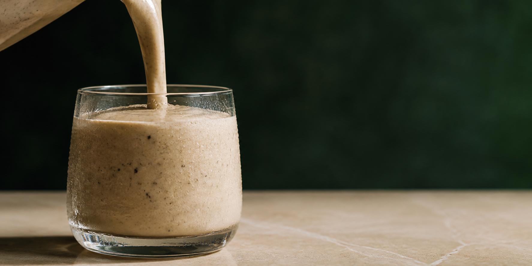 Thick, lightly speckled GymPlant meal pouring into a chilled glass